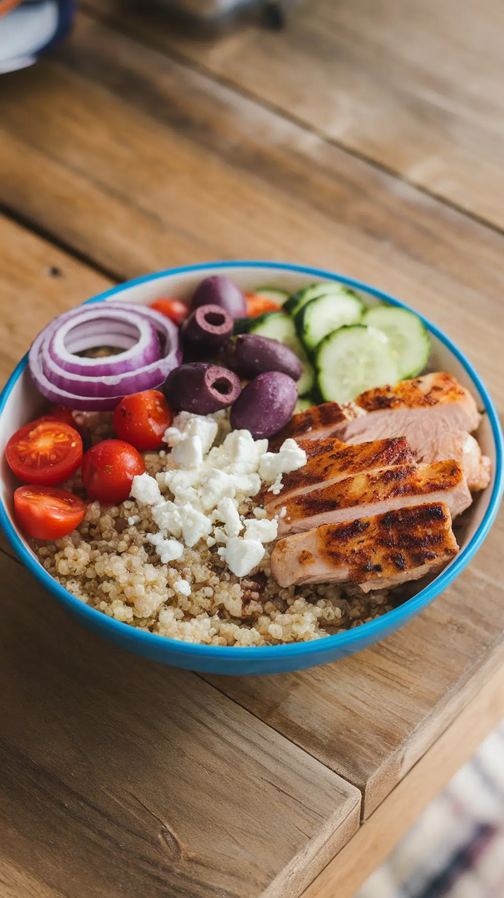 A colorful Mediterranean Chicken Quinoa Bowl with grilled chicken, quinoa, cherry tomatoes, cucumbers, red onions, olives, and feta cheese.