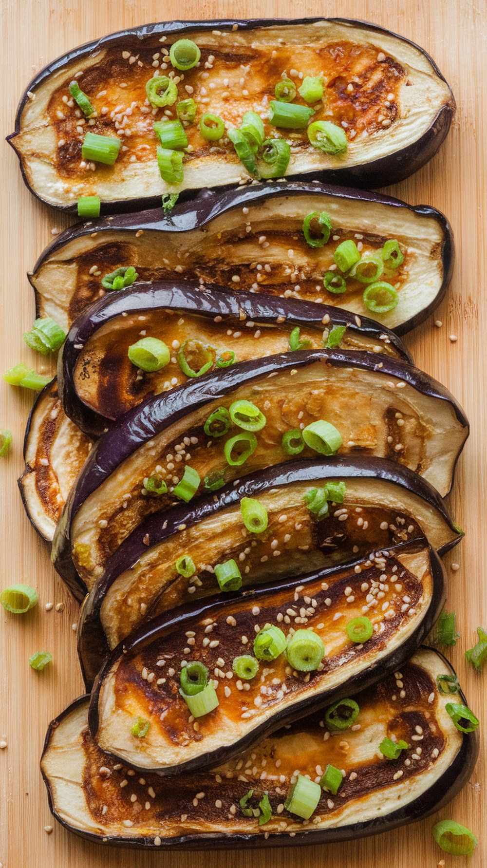 Miso-glazed eggplant slices topped with green onions and sesame seeds on a wooden board.