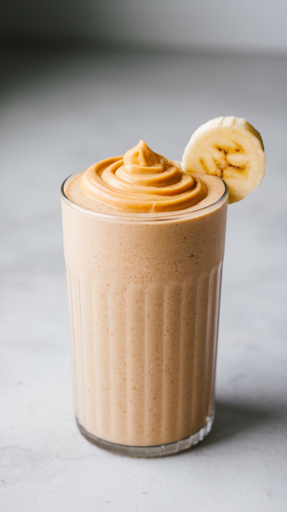 A creamy Peanut Butter Banana Protein Shake topped with a swirl of peanut butter and a slice of banana.
