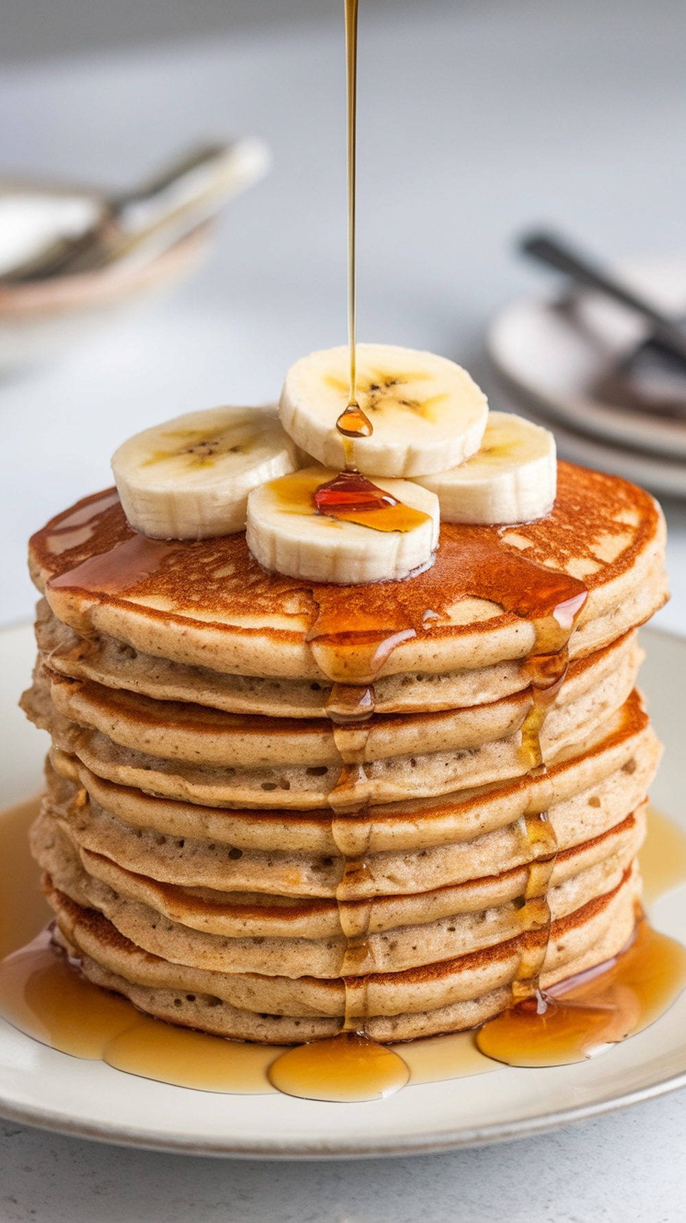 Stack of banana oatmeal pancakes topped with banana slices and syrup