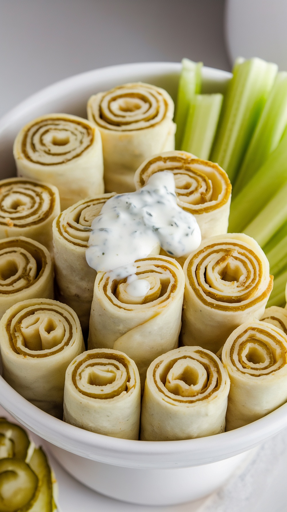 Bowl of creamy ranch pickle roll up dip with rolled tortillas and celery sticks