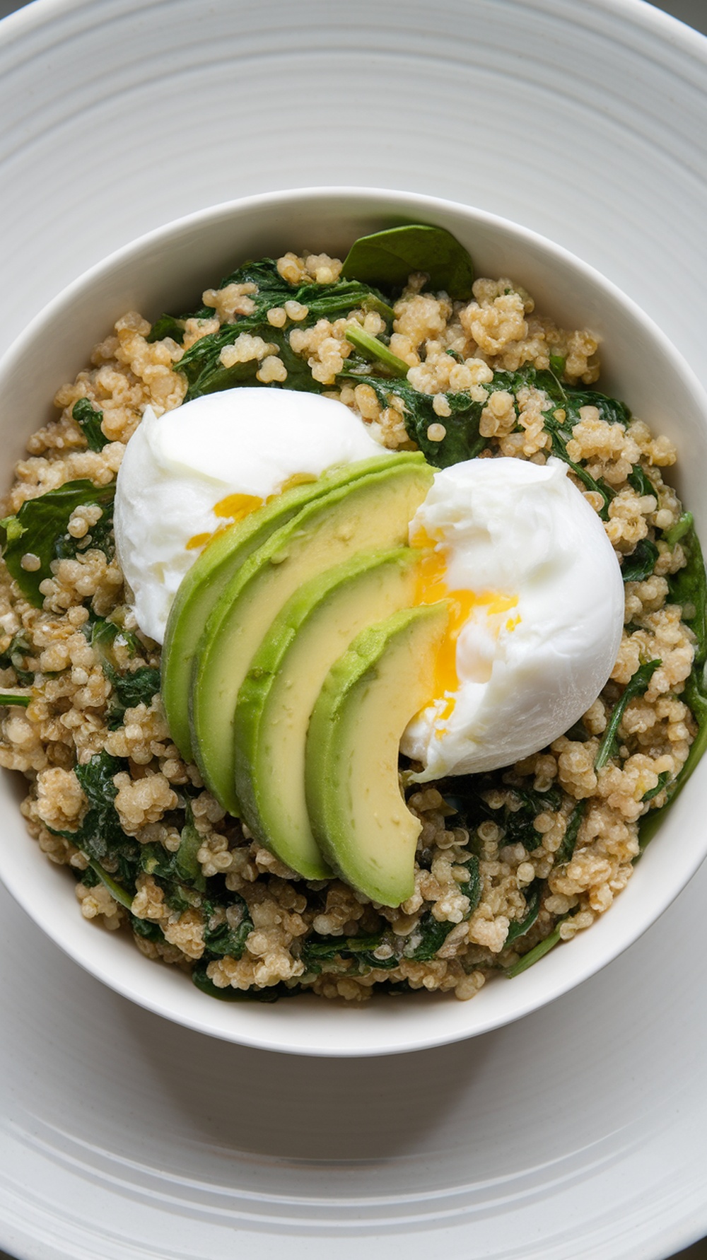 A healthy breakfast bowl with quinoa, spinach, poached eggs, and avocado slices.