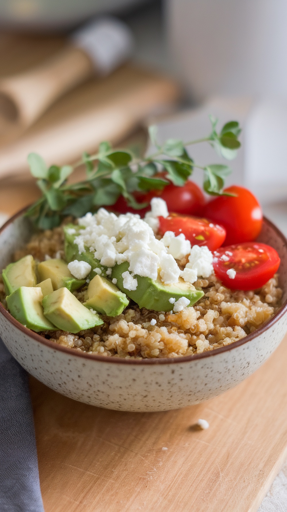 A bowl of savory breakfast quinoa topped with avocado, cherry tomatoes, and feta cheese.