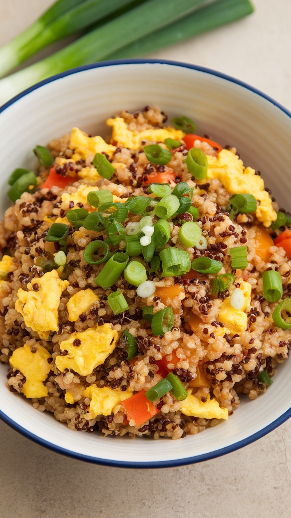A bowl of quinoa fried rice topped with green onions and colorful vegetables.