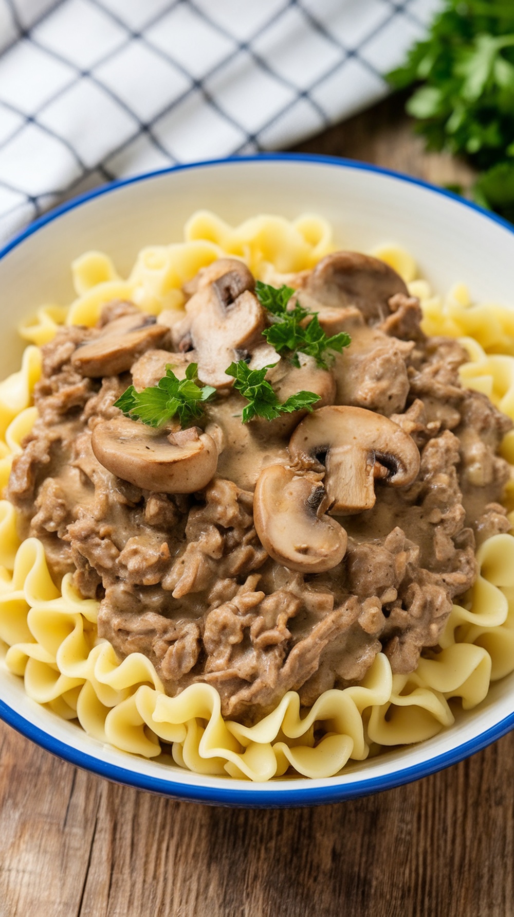 A bowl of beef stroganoff served over egg noodles, garnished with parsley and mushrooms.