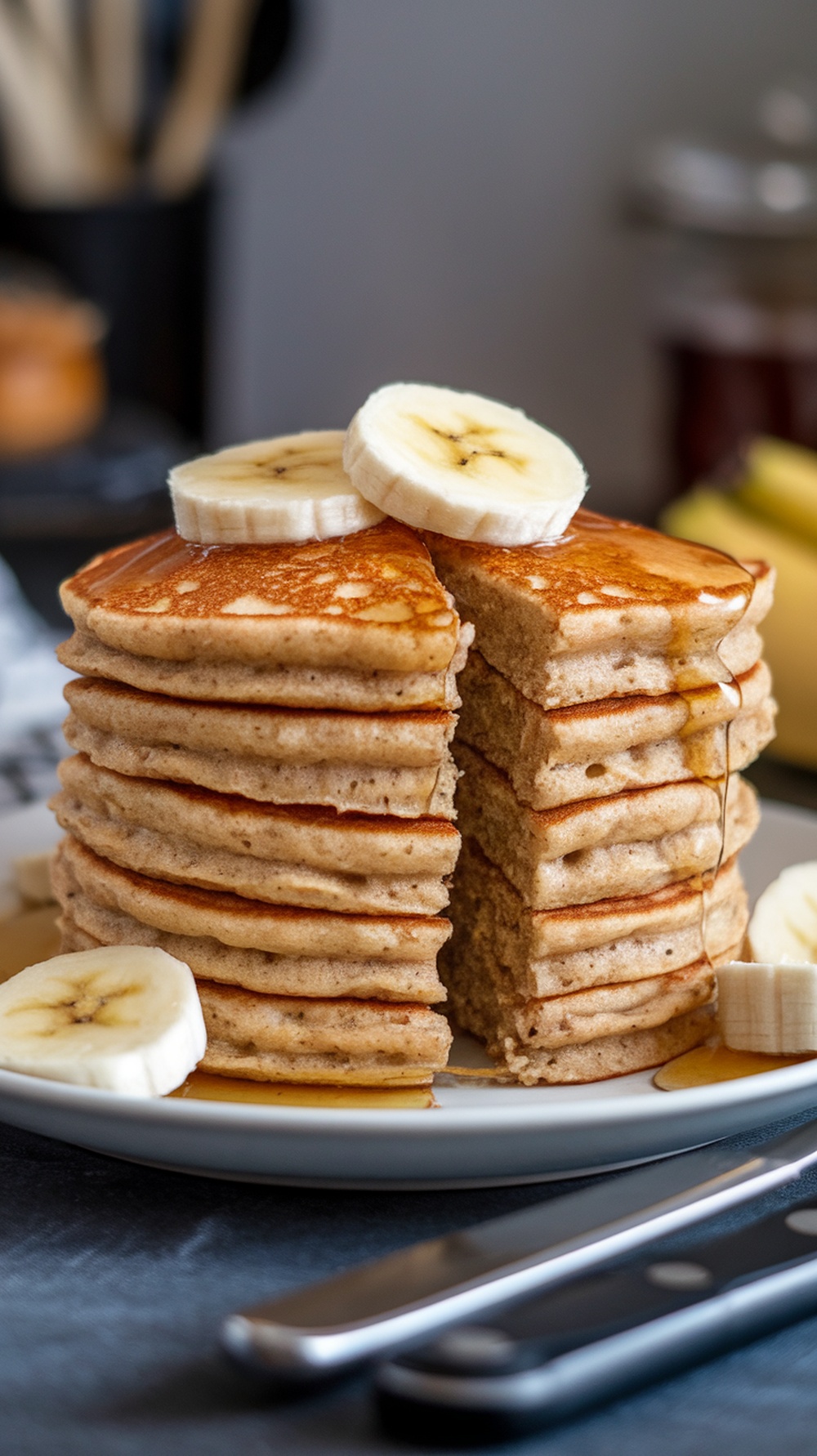 A stack of fluffy banana oat protein pancakes topped with banana slices and syrup.